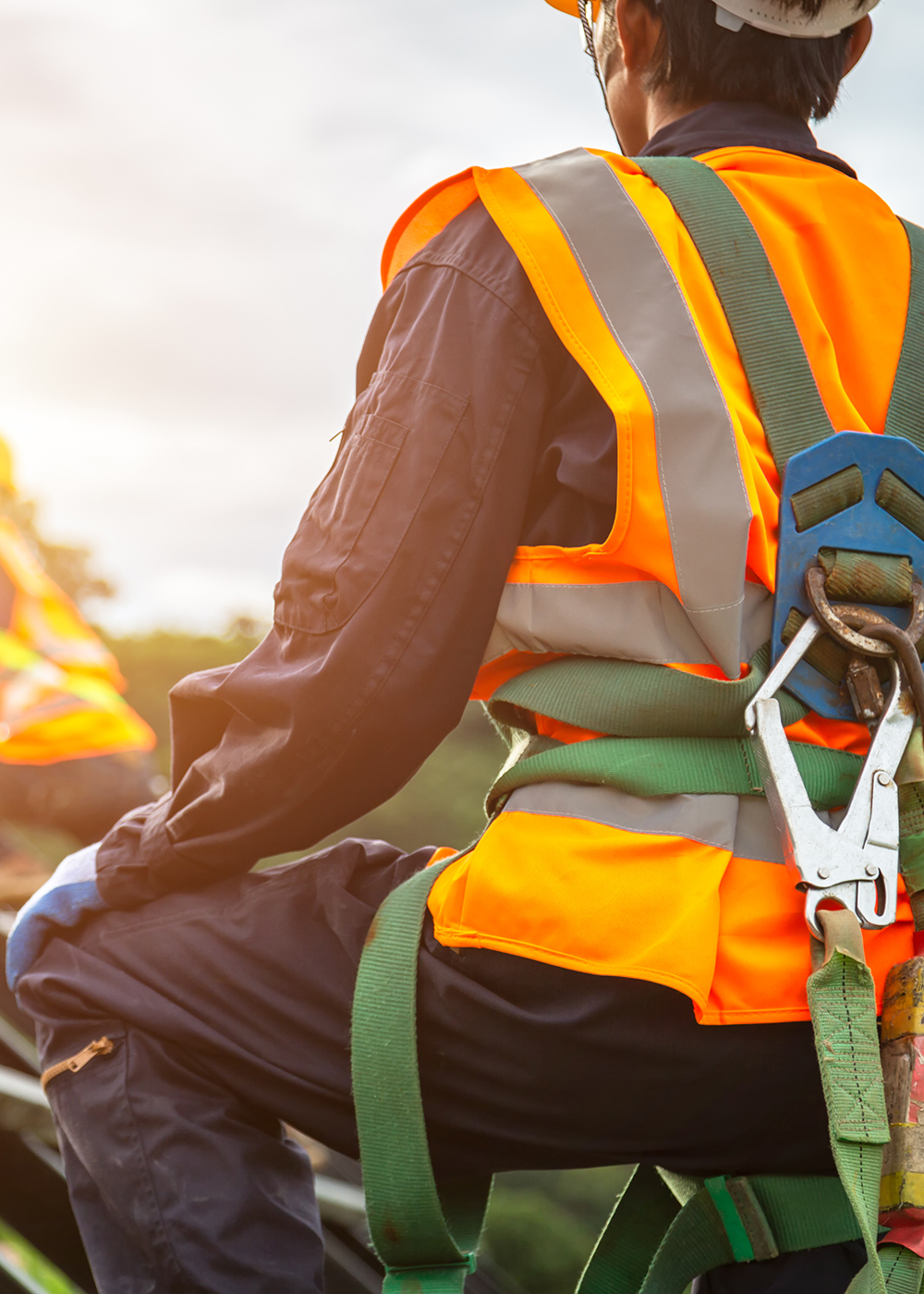 Construction worker in orange safety vest and green harness while on the roof of a building.