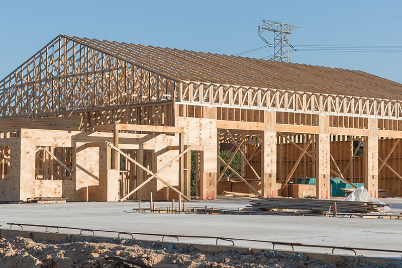 Wood frame house under construction with foundation in Humble, Texas, USA. New stick built framing one floor commercial building clear blue sky. Pile of beams, log, sand, gravel. Industrial background