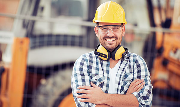 Young male construction worker with construction site behind him.