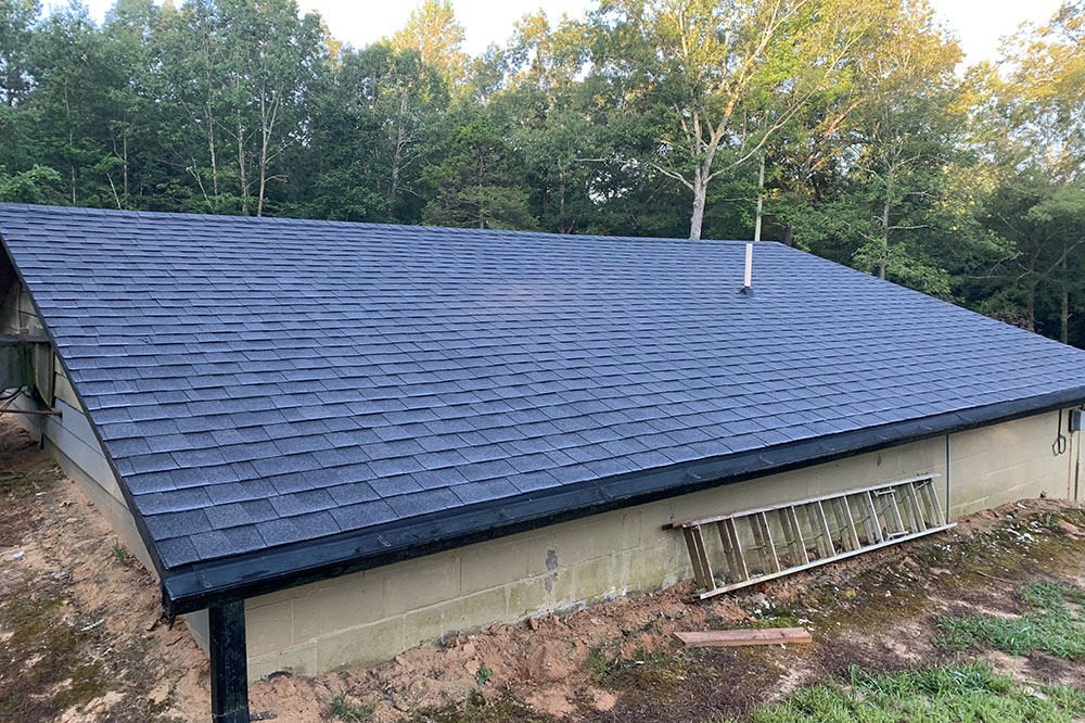 The side of a black shingled roof of a small cement block building.