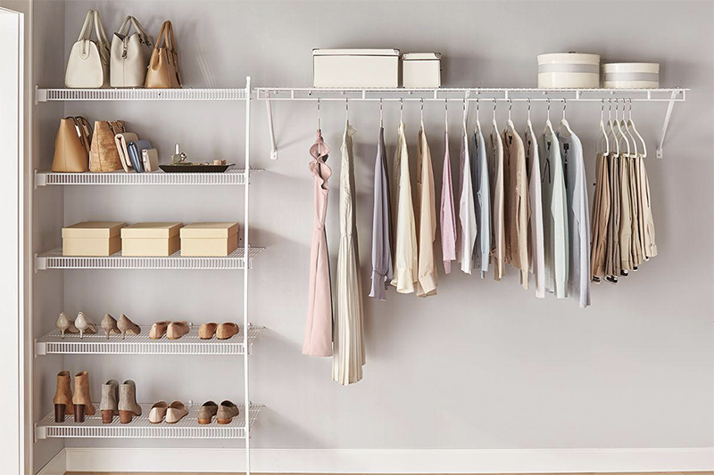 A well-organized closet with several hanging shirts and accessories stacked on a white wire organization shelf.