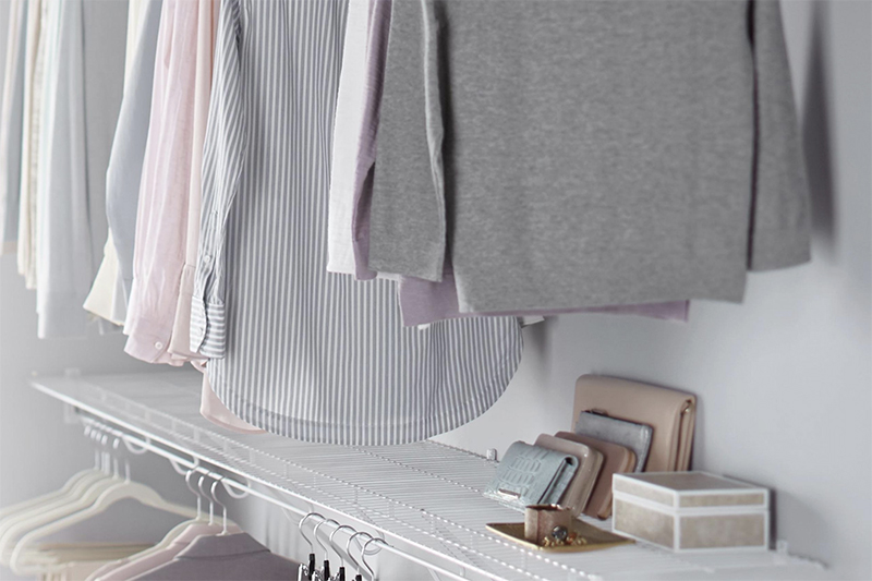 A well-organized closet with several hanging shirts and accessories stacked on a white wire organization shelf.