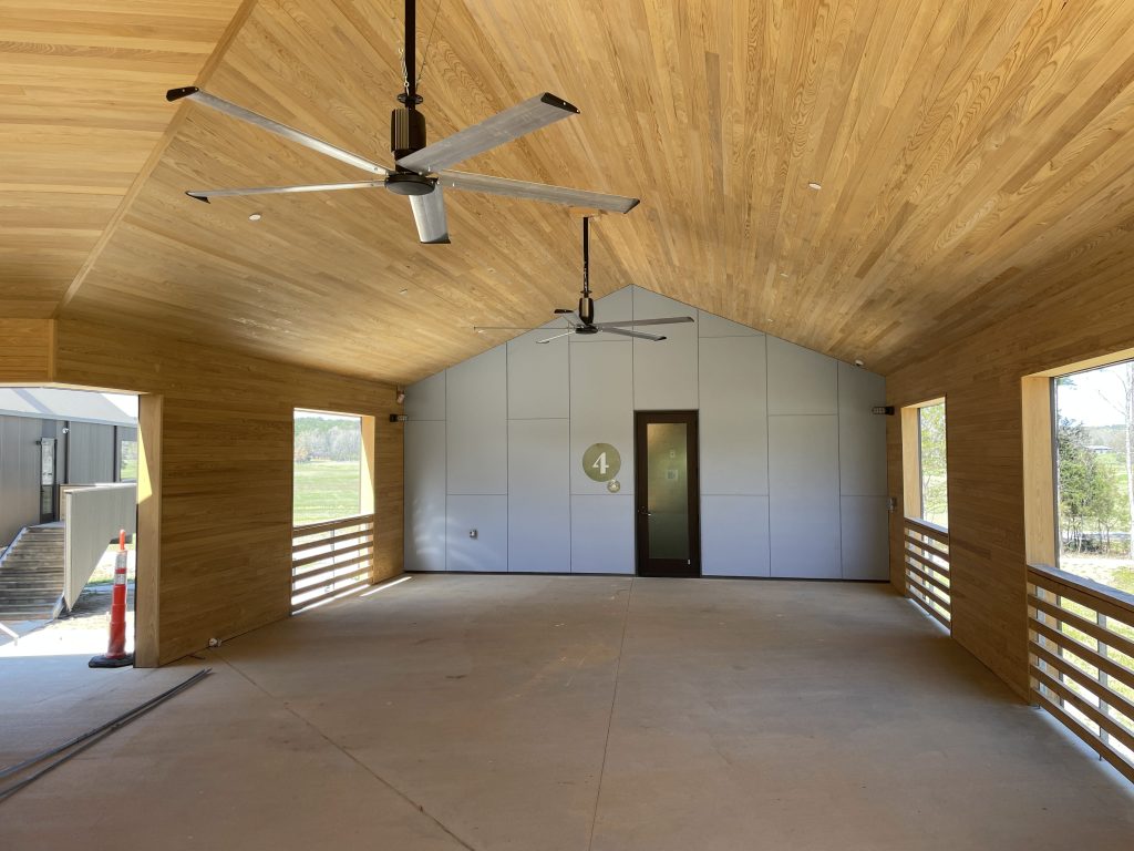 Interior of a new open hall with wooden walls and ceiling with two ceiling fans. A glass door is in the middle with a number four sign on the side of the door.